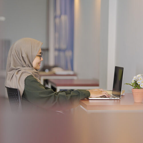 Young woman wearing a head scarf sitting at a desk working on a laptop